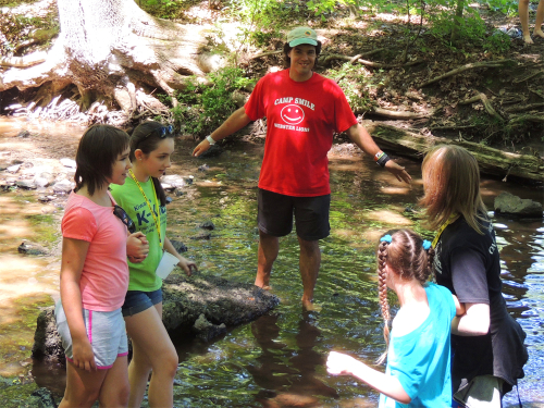Counselors assisting campers as they walk through the water in a shallow creek