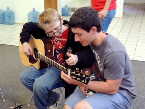 Counselor teaching a camper how to play guitar 