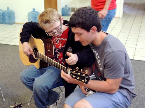 Counselor teaching a camper how to play guitar